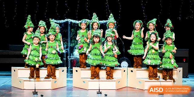 Young students dressed in festive green tree costumes perform during a holiday school show at Xi_an Hanova International School.