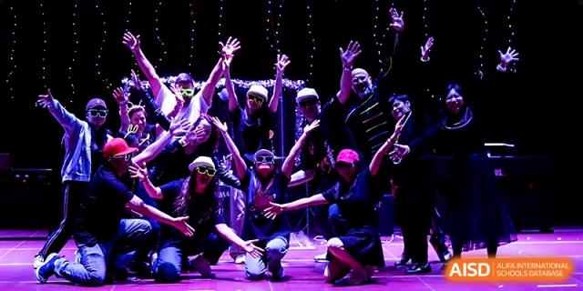 A high-energy group of students and teachers perform with raised arms under purple stage lights at Xi_an Hanova International School.