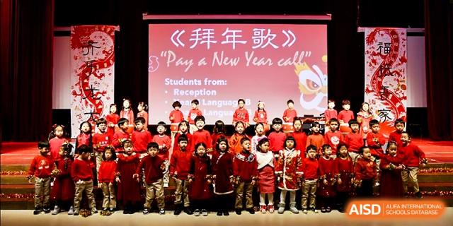 A large choir of young students in traditional red outfits performs a New Year song on stage at Xi_an Hanova International School.