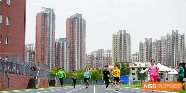 Students participate in a competitive track race on the outdoor sports field with city buildings behind Xi_an Hanova International School.