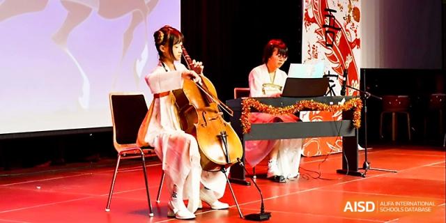 A student in traditional attire plays the cello accompanied by a pianist during a formal recital at Xi_an Hanova International School.
