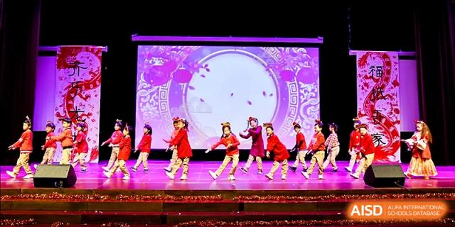 A group of young dancers in red costumes performs a choreographed routine on a brightly lit stage at Xi_an Hanova International School.