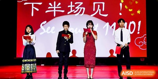 Two student presenters, a boy in a suit and a girl in a red dress, host a school event on stage at Xi_an Hanova International School.