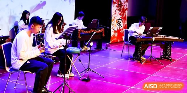 Students perform a musical piece using a keyboard and string instruments under purple stage lights at Xi_an Hanova International School.