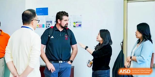 A male and female faculty member engage in a professional discussion in a hallway at Beijing Xicheng Academy.