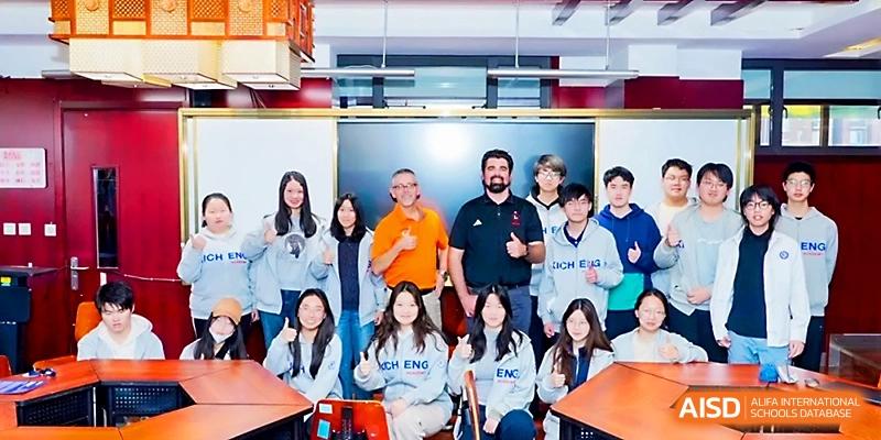 A group of students and teachers pose for a cheerful group photo inside a classroom at Beijing Xicheng Academy.
