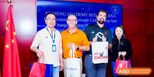 Three men stand together holding gift bags during an official school event or visit at Beijing Xicheng Academy.
