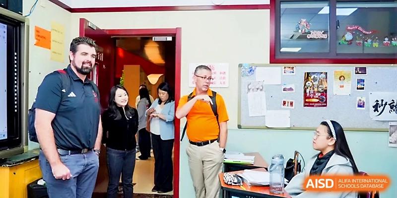 A faculty member stands in a doorway while observing classroom activities and interactions at Beijing Xicheng Academy.