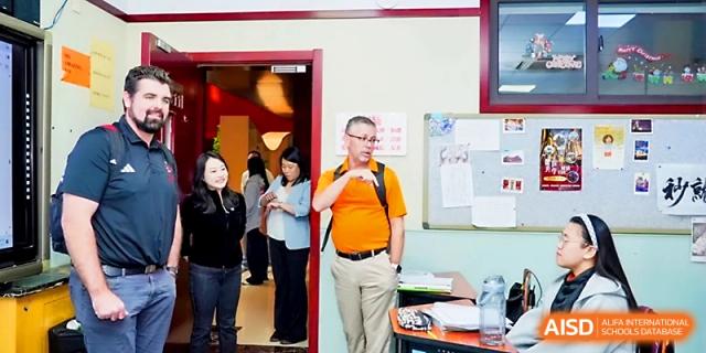 A faculty member stands in a doorway while observing classroom activities and interactions at Beijing Xicheng Academy.