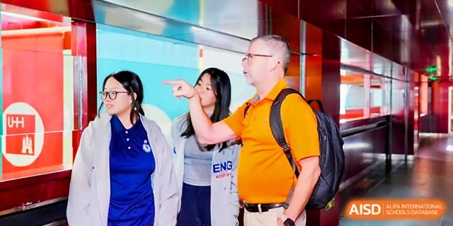 A teacher in an orange shirt gestures while explaining a concept to students in a lab at Beijing Xicheng Academy.