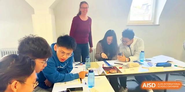 A teacher stands by as students work together on a hands-on assignment at their desks at Beijing Xicheng Academy.