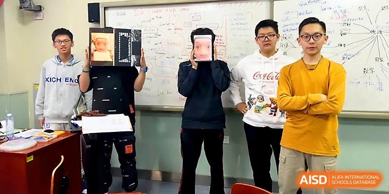 Three students stand in a classroom, with two holding up books to cover their faces during a fun activity at Beijing Xicheng Academy.