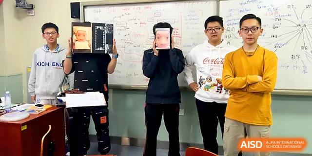 Three students stand in a classroom, with two holding up books to cover their faces during a fun activity at Beijing Xicheng Academy.