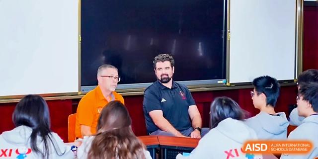 Two instructors sit at the front of a classroom during a collaborative seminar or Q&A at Beijing Xicheng Academy.
