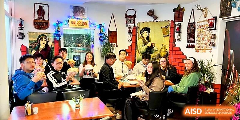 Students and teachers gather around a dining table in a cozy, decorated room for a social gathering at Beijing Xicheng Academy.