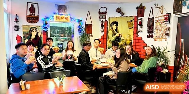 Students and teachers gather around a dining table in a cozy, decorated room for a social gathering at Beijing Xicheng Academy.