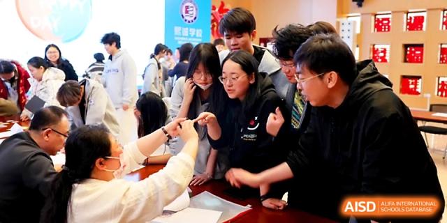 A large group of students gathers excitedly around a table to participate in a hands-on group project at Beijing Xicheng Academy.