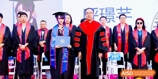 A student receives their diploma from a faculty member on stage during a graduation ceremony at Beijing Xicheng Academy.