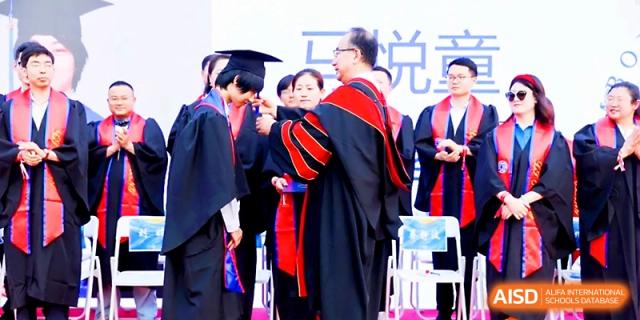 A faculty member adjusts a student's graduation cap during a formal commencement ceremony at Beijing Xicheng Academy.