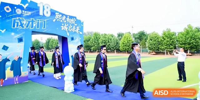 Graduates in black and blue gowns walk across the outdoor track during a formal graduation procession at Beijing Xicheng Academy.