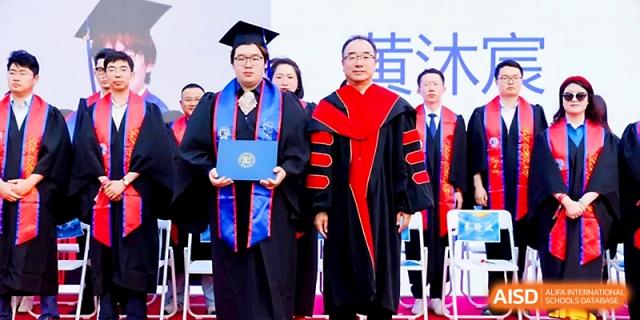 A student in a graduation gown poses with a faculty member while holding their diploma at Beijing Xicheng Academy.