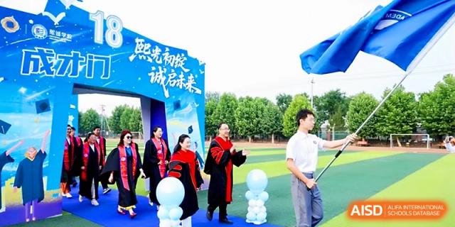 Graduates and faculty walk through a blue ceremonial archway during an outdoor celebration at Beijing Xicheng Academy.