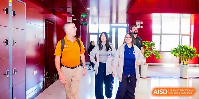 A teacher in an orange shirt walks with students down a modern school hallway at Beijing Xicheng Academy.