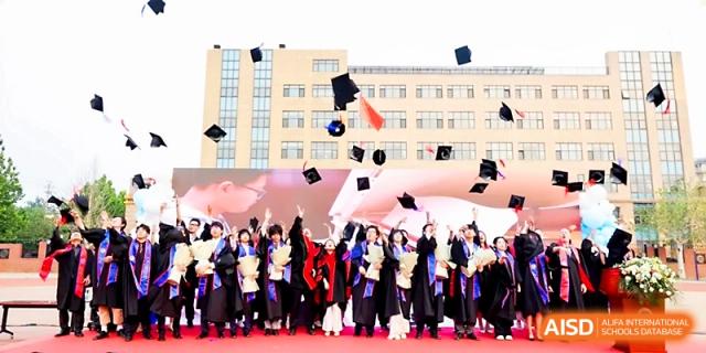 Graduates joyfully throw their caps into the air in front of the school building during commencement at Beijing Xicheng Academy.