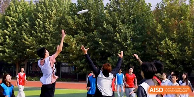 Students reach up to catch a flying disc during an active game of ultimate frisbee on the school grounds at Beijing Xicheng Academy.