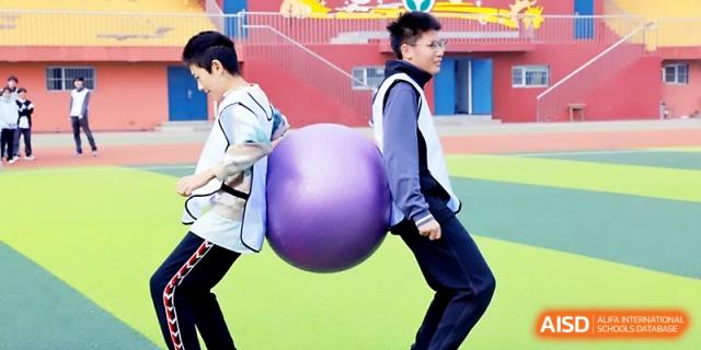 Two students work together to carry a large yoga ball between their backs during an outdoor sports event at Beijing Xicheng Academy.