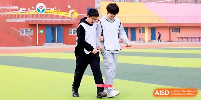 Two students participate in a three-legged race during a fun sports competition on the green outdoor field at Beijing Xicheng Academy.