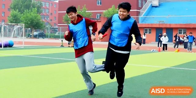 Two boys in blue vests race together across the field during a spirited outdoor athletics competition at Beijing Xicheng Academy.