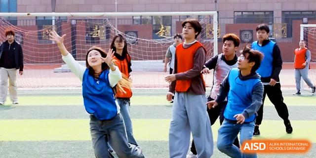 A group of students in athletic vests prepares for a team activity on the outdoor sports field at Beijing Xicheng Academy.