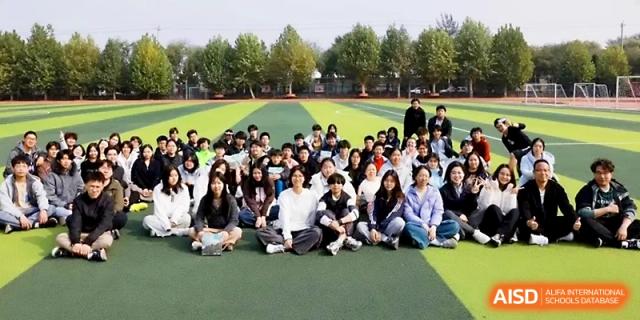 A large group of students sits together on the green sports field for a commemorative group photo at Beijing Xicheng Academy.