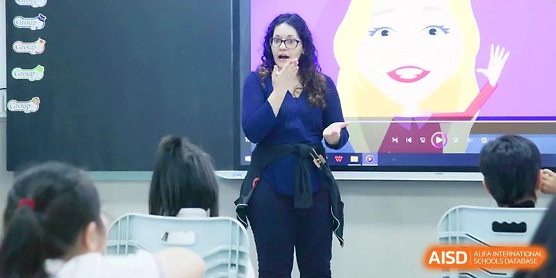 An expressive teacher gestures while standing in front of a digital screen, leading an interactive presentation for her class at Yangjiang Yangdong Eone school.