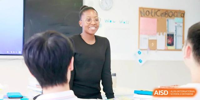 A smiling female teacher with glasses stands in a bright classroom, engaging warmly with her students during a lesson at Yangjiang Yangdong Eone school.