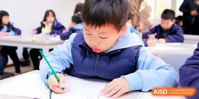 A student in a blue vest concentrates on his schoolwork, carefully writing in his notebook during a quiet study session at Yangjiang Yangdong Eone school.