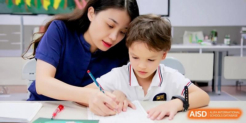 A female teacher leans in to provide one-on-one guidance to a young boy as he practices his writing at his desk at Yangjiang Yangdong Eone school.