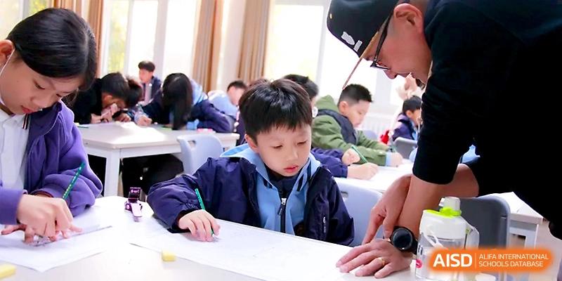 A teacher provides hands-on assistance to a student working at a large desk in a bustling, productive classroom environment at Yangjiang Yangdong Eone school.