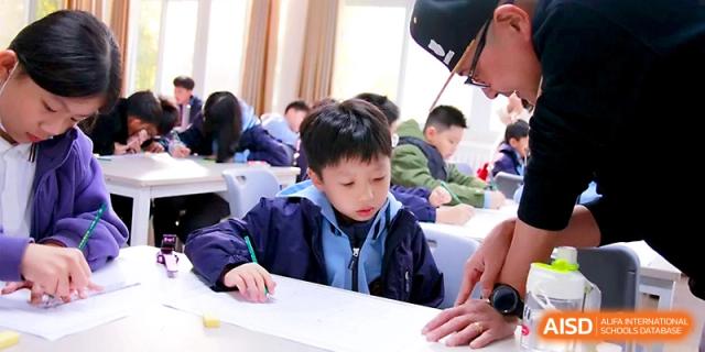 A teacher provides hands-on assistance to a student working at a large desk in a bustling, productive classroom environment at Yangjiang Yangdong Eone school.