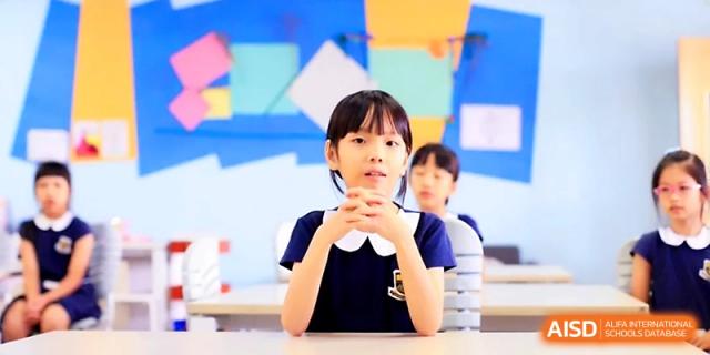 A young girl in a navy uniform sits at her desk, listening attentively to her teacher at Yangjiang Yangdong Eone school.
