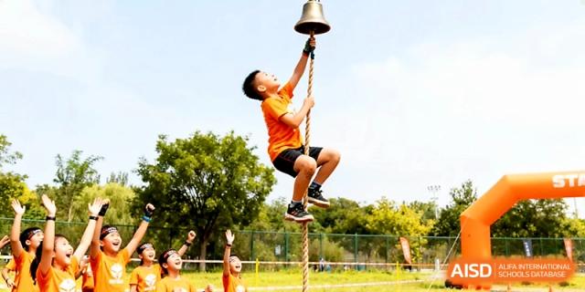 A determined boy climbs a rope to ring the bell at the top during an outdoor physical education challenge at Yangjiang Yangdong Eone school.