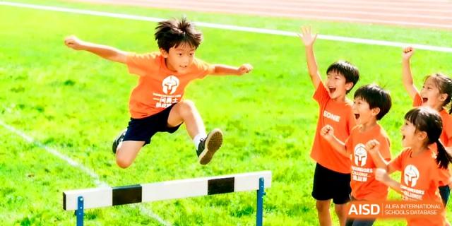 A young student in an orange shirt jumps over a hurdle during a track and field competition on the school grounds at Yangjiang Yangdong Eone school.