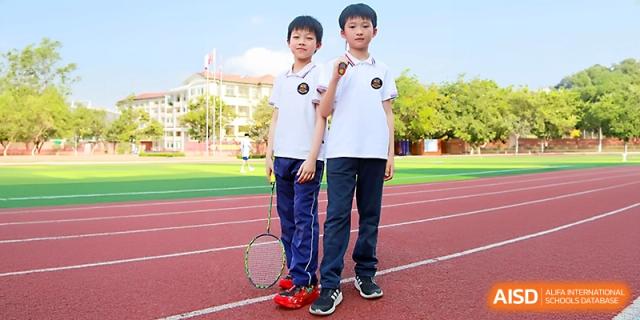 Two young boys stand on the red running track holding a badminton racket, ready for a sports match at Yangjiang Yangdong Eone school.