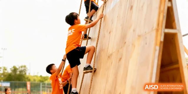 Students demonstrate teamwork and strength as they climb a wooden wall using ropes during an obstacle course at Yangjiang Yangdong Eone school.