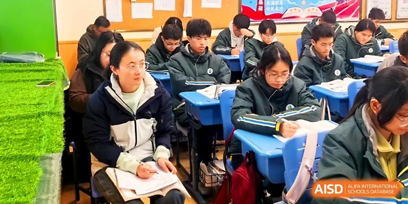 Students in dark green winter uniforms focus on their notebooks during a quiet study session in a bright classroom at Yangzhou Shuren High School.
