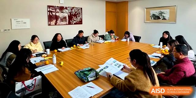 A group of educators participates in a training workshop, seated at a wooden table with instructional materials at Yangzhou Shuren High School.