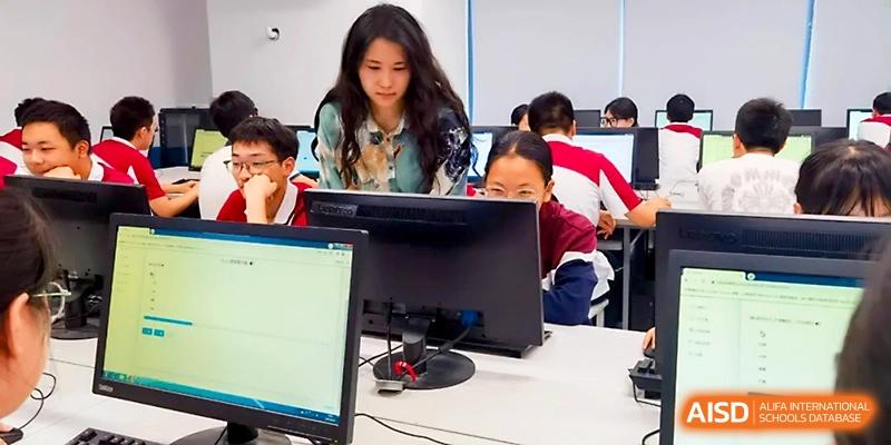 A female teacher leans in to provide one-on-one guidance to a student working on a computer during a lab session at Yangzhou Shuren High School.