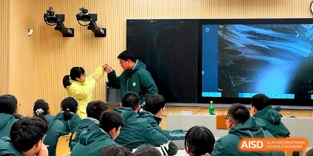 A teacher in a green jacket leads a demonstration at the front of a classroom using a large digital screen at Yangzhou Shuren High School.