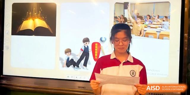 A female student stands in front of a digital display, reading aloud from a paper during a classroom presentation at Yangzhou Shuren High School.